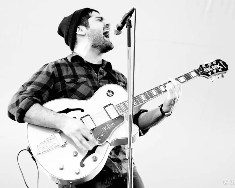 Black and white photo of Sal playing a guitar and singing into a microphone.