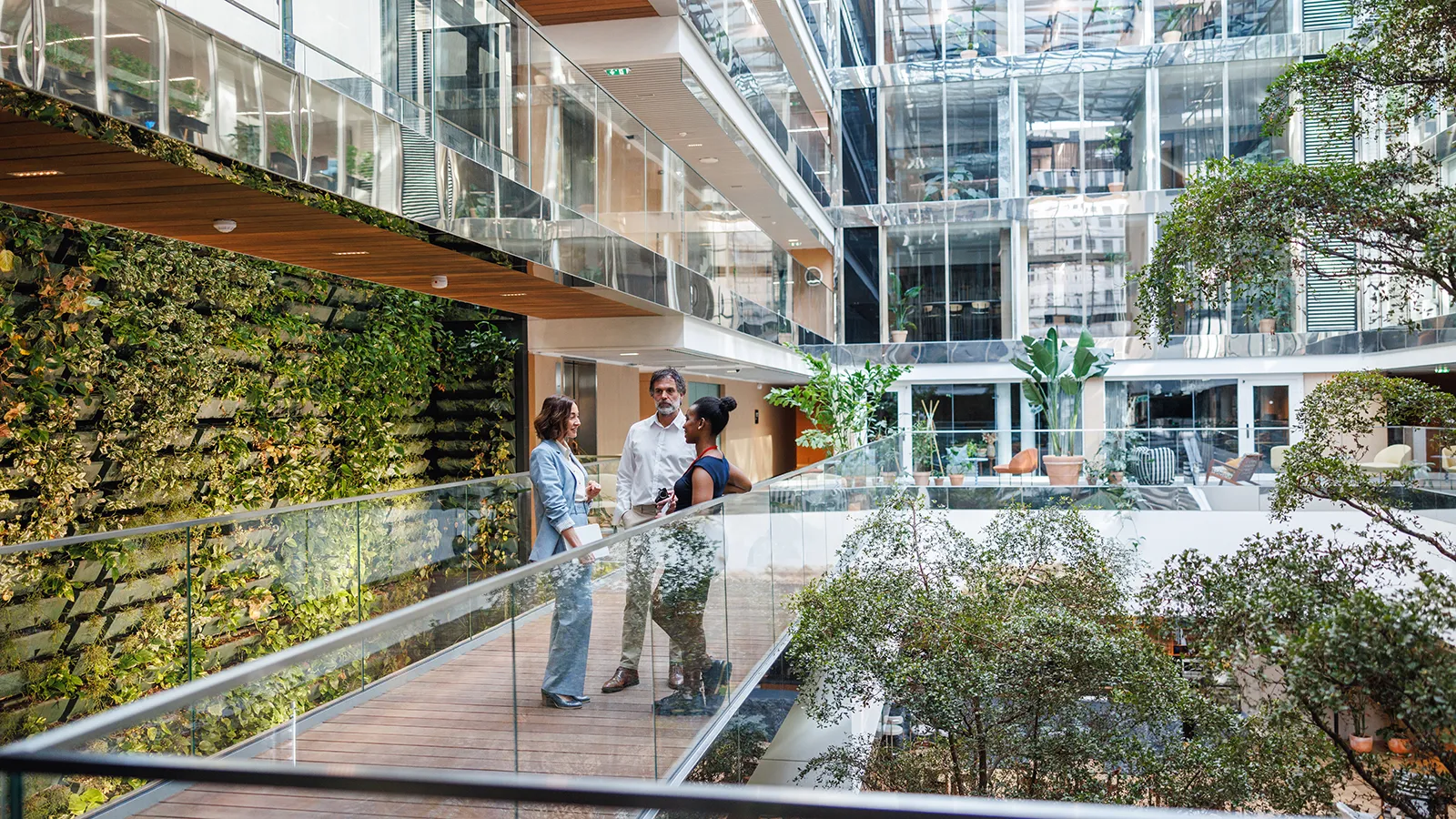 A completed, thriving indoor atrium filled with lush plants, ample sunlight, and people working comfortably, demonstrating the value of properly planned biophilic design architecture.