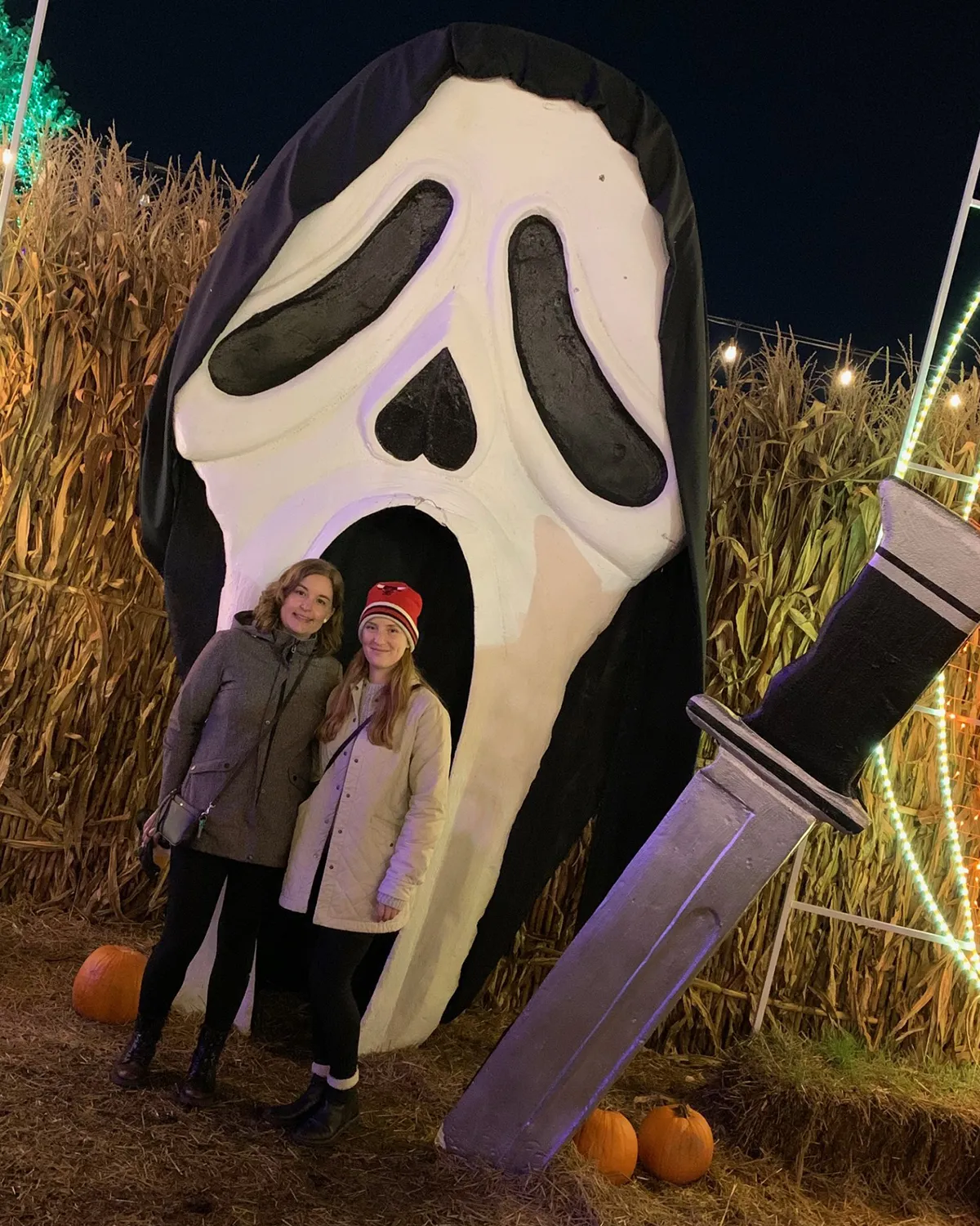 Photo of Tori and a friend standing in front of a giant Ghostface (Scream) mask.